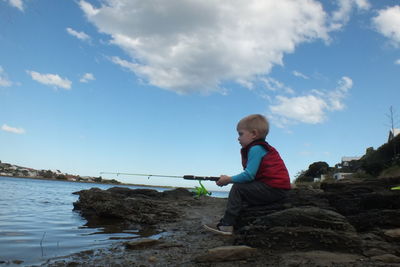 Full length of boy fishing in river against sky