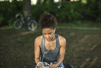 Close-up of woman sitting on bench listening music in park