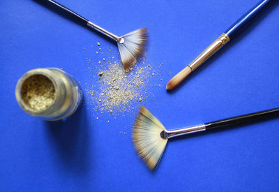 Directly above shot of make-up brushes with glitter on blue table