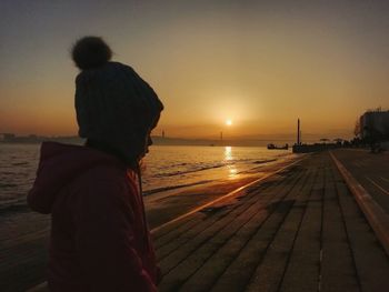 Rear view of woman standing on beach at sunset