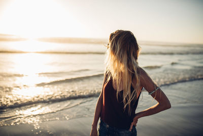 Rear view of woman standing at beach during sunset