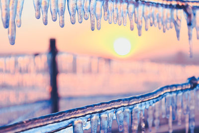 Close-up of icicles hanging against sky during sunset