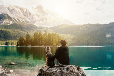 Rear view of man sitting on rock by lake