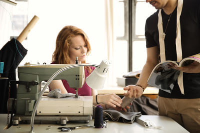 Fashion designer giving spool to coworker while working at workshop