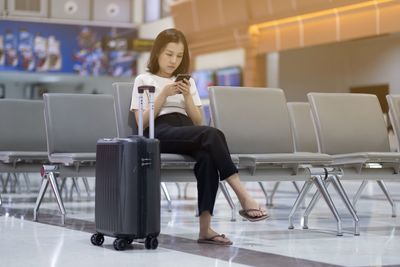 Woman using phone while sitting on chair at airport