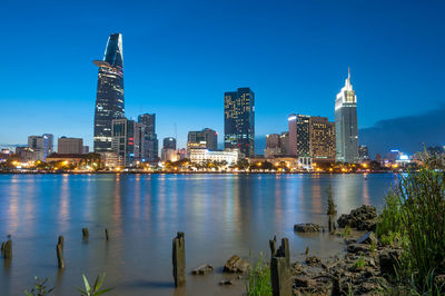 Illuminated buildings by river against sky in city