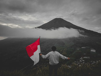 Rear view of men flag on mountain against sky