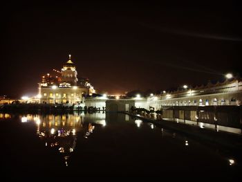 Illuminated building by lake against sky in city at night
