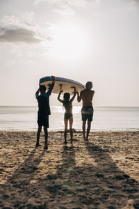 Father and children carrying surfboard while walking towards sea at beach