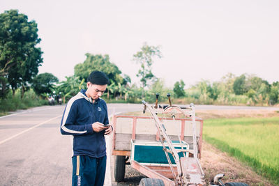 Young man using mobile phone while standing on tree