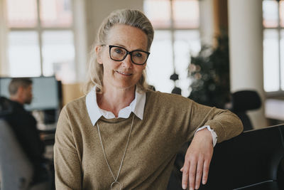 Portrait of smiling female entrepreneur with eyeglasses leaning on chair at workplace