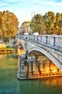 Arch bridge over river against sky during autumn