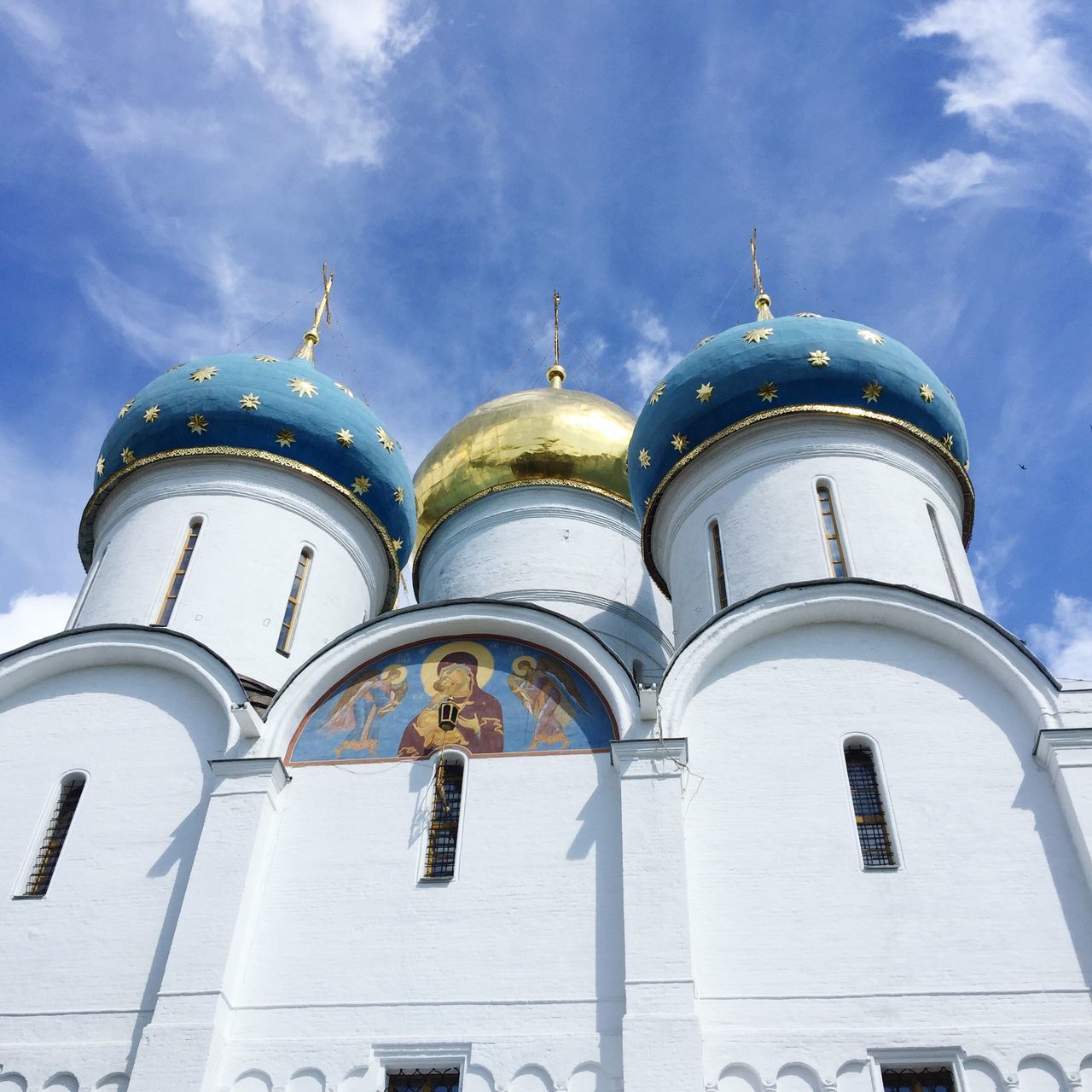 low angle view, architecture, religion, place of worship, spirituality, built structure, building exterior, sky, blue, window, church, arch, cloud, travel destinations, outdoors, sunny, day, high section, facade, cloud - sky, famous place, history, spire, no people, architectural feature