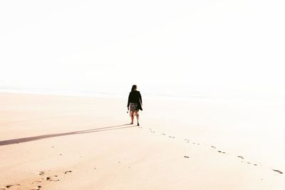 Rear view of woman walking at beach during sunny day