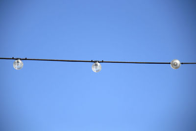 Low angle view of light bulbs on cable against clear blue sky