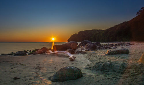 Rocks on beach against sky during sunset