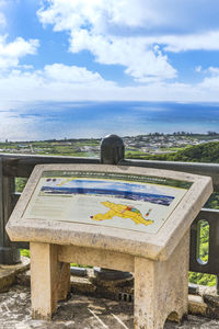 Text on bench by sea against sky