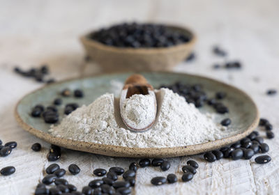 Ceramic plate with black beans flour and dried beans with a wooden spoon 