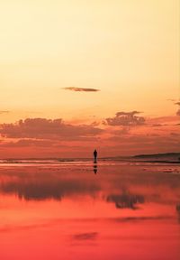 Distant view of silhouette person on beach against sky during sunset