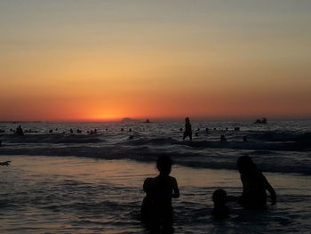 Silhouette people on beach against sky during sunset