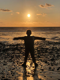 Silhouette child standing on beach against sky during sunset