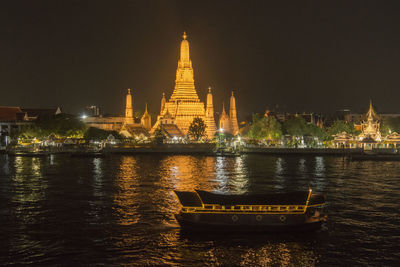 Illuminated temple by river against sky at night