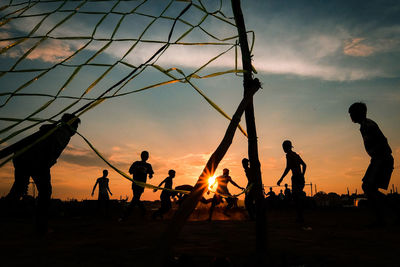 Silhouette people playing soccer against sky during sunset