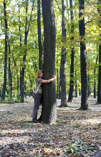 Side view of senior woman embracing tree trunk in forest