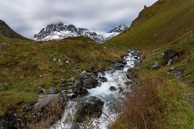 Scenic view of stream flowing amidst rocks against sky