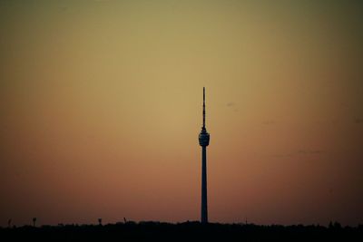 Silhouette communications tower in city against sky during sunset