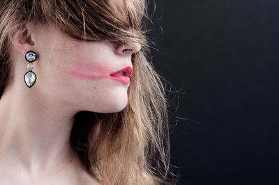 Close-up of woman wearing earring against black background