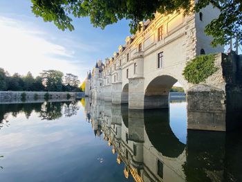 Arch bridge over lake by buildings against sky