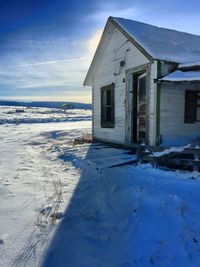 House by snowy field against sky during sunny day