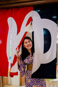 Portrait of smiling young woman standing against red wall