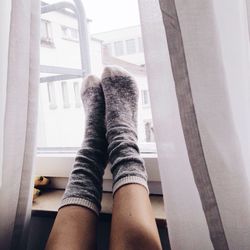 Low section of woman wearing socks against window