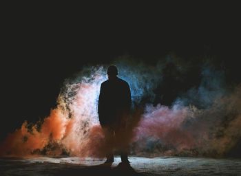 Silhouette man standing amidst smoke against sky during night