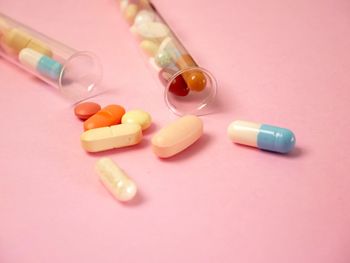 Medicines spilling from test tubes over pink background