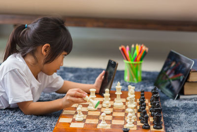 Girl holding mobile phone playing chess at home