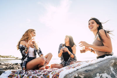 Friends enjoying drinks at beach against clear sky during summer