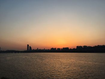 Silhouette buildings by sea against sky during sunset