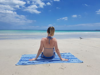 Rear view of woman wearing bikini while sitting on picnic blanket at beach during summer