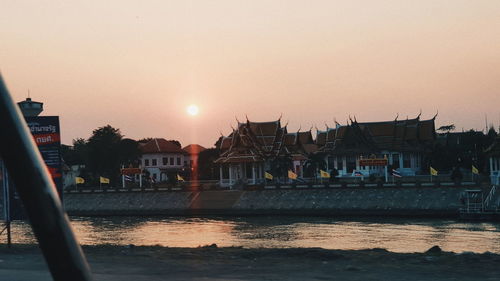 River by houses and buildings against clear sky during sunset