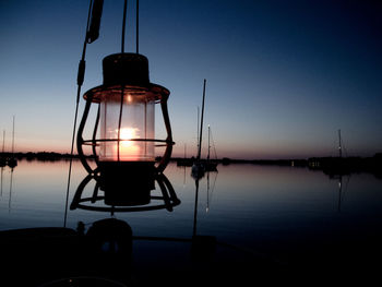 Reflection of illuminated lamp on lake against sky during sunset