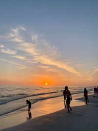 People at beach against sky during sunset