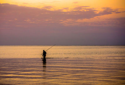 Silhouette man fishing in sea against cloudy sky