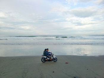 Man riding motorcycle on beach against sky