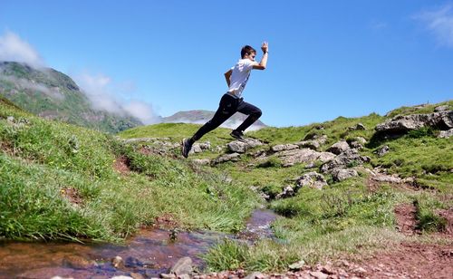 Young woman jumping on rock against sky