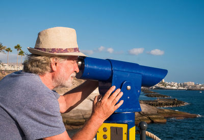Man looking through coin-operated binoculars at sea 