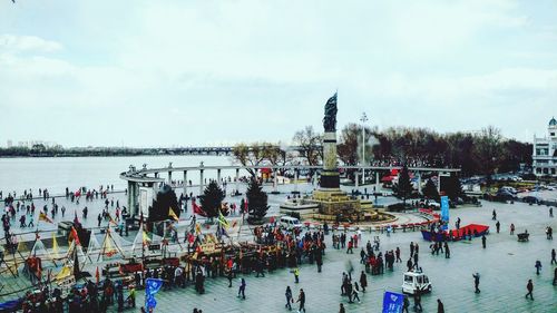 High angle view of people by monument on street against cloudy sky