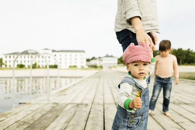 Portrait of baby girl standing with family on pier at beach against clear sky